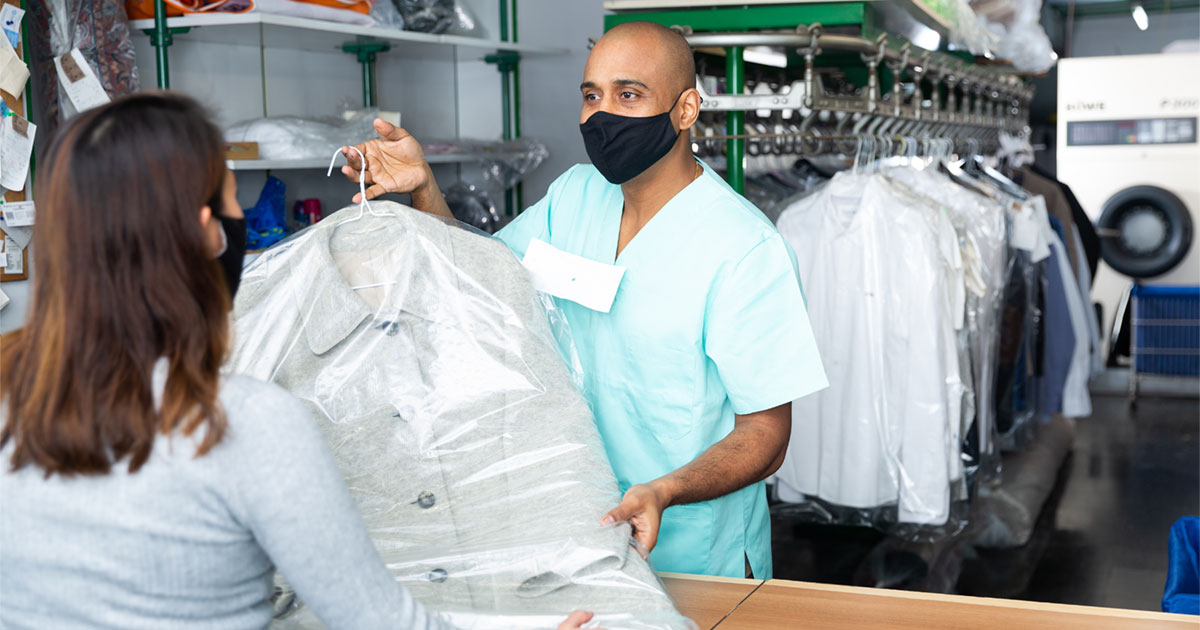drycleaner with mask handing clean clothes to customer