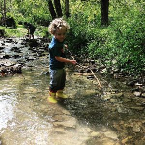 Boy standing in a creek with long branch in hands
