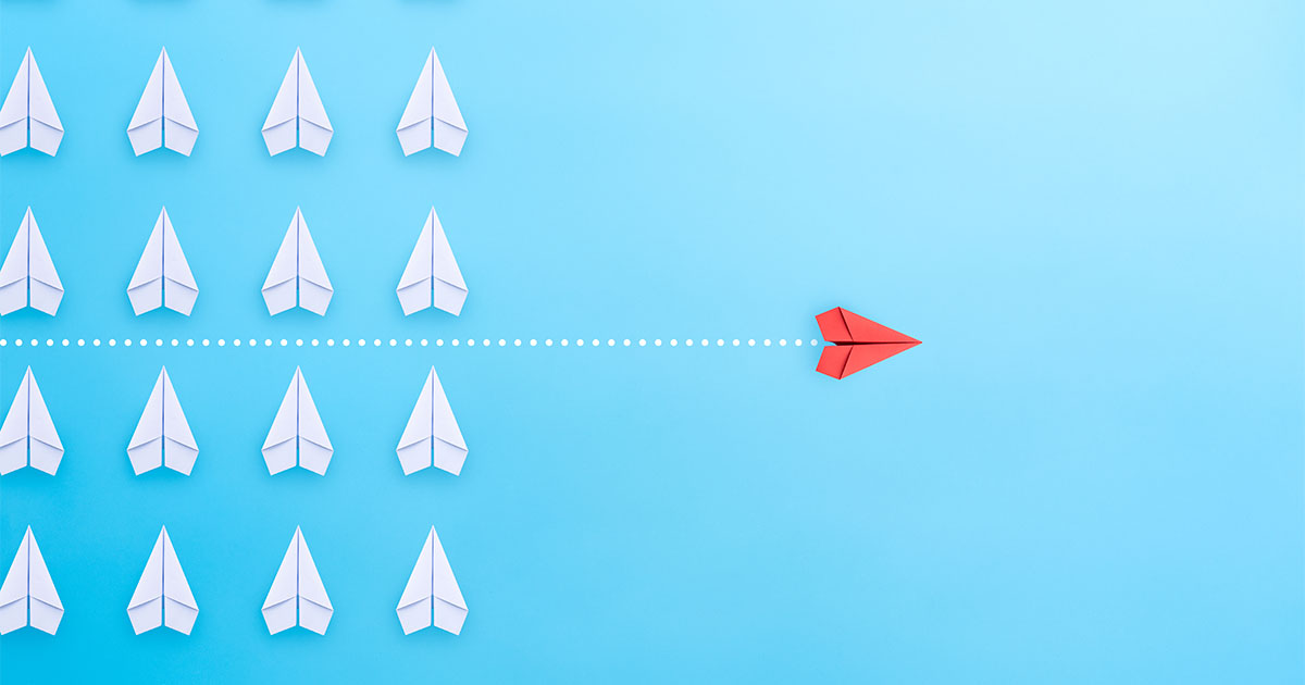 A red paper air plane moving forward with a new strategy away from a group of white paper air planes