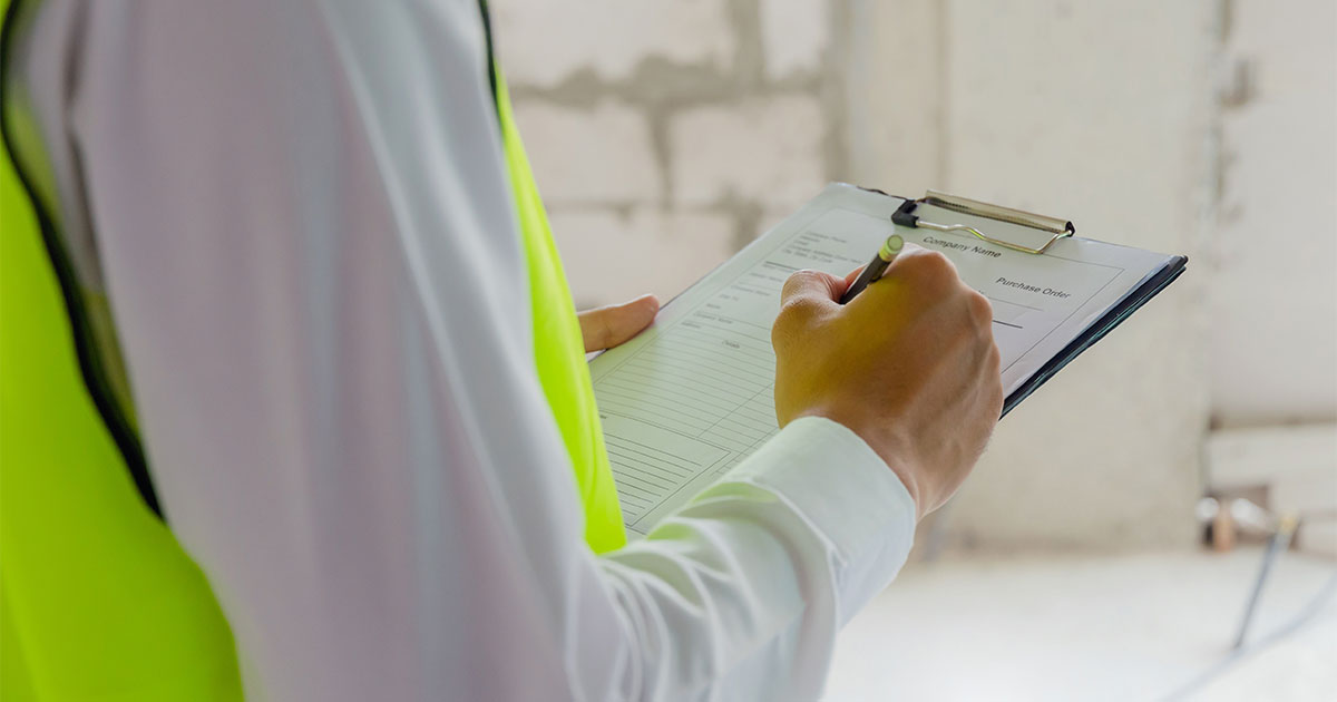 Environmental consultant wearing yellow safety vest writing notes on a clipboard during a Phase I Environmental Site Assessment