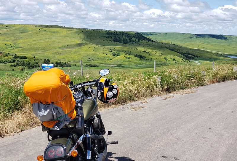 Motorcycle on a remote road overlooking a grassy, sunlit valley