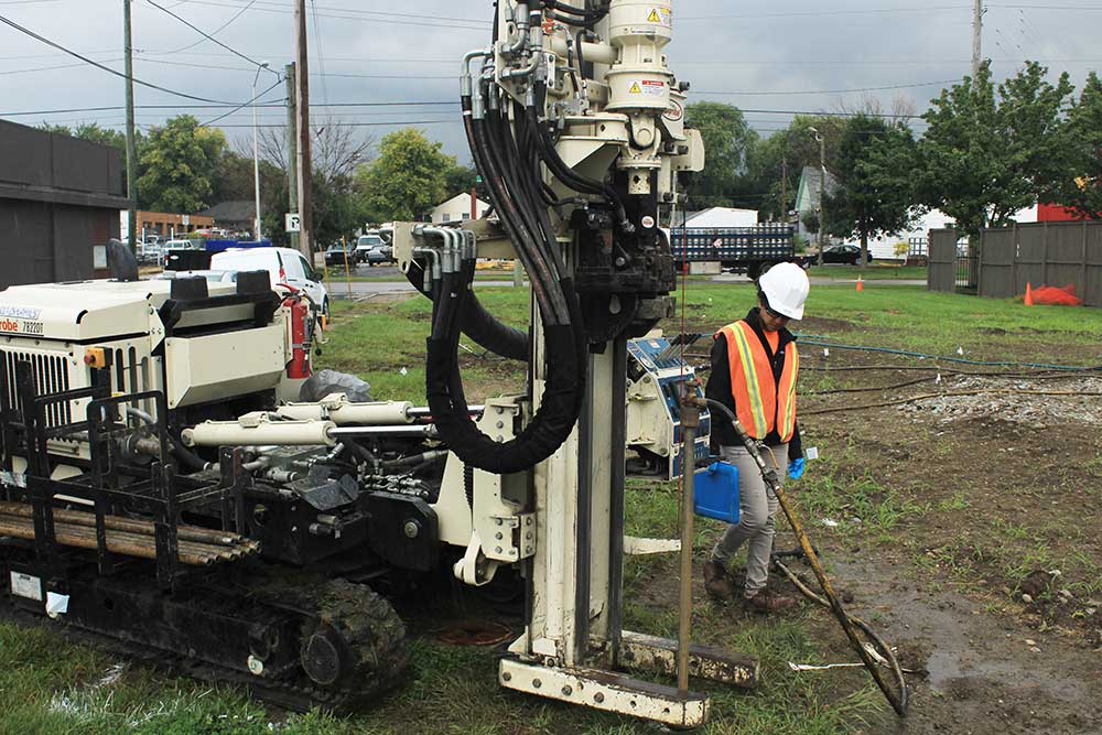 Environmental consultant in full protective gear overseeing an in-situ remediation application using a drill