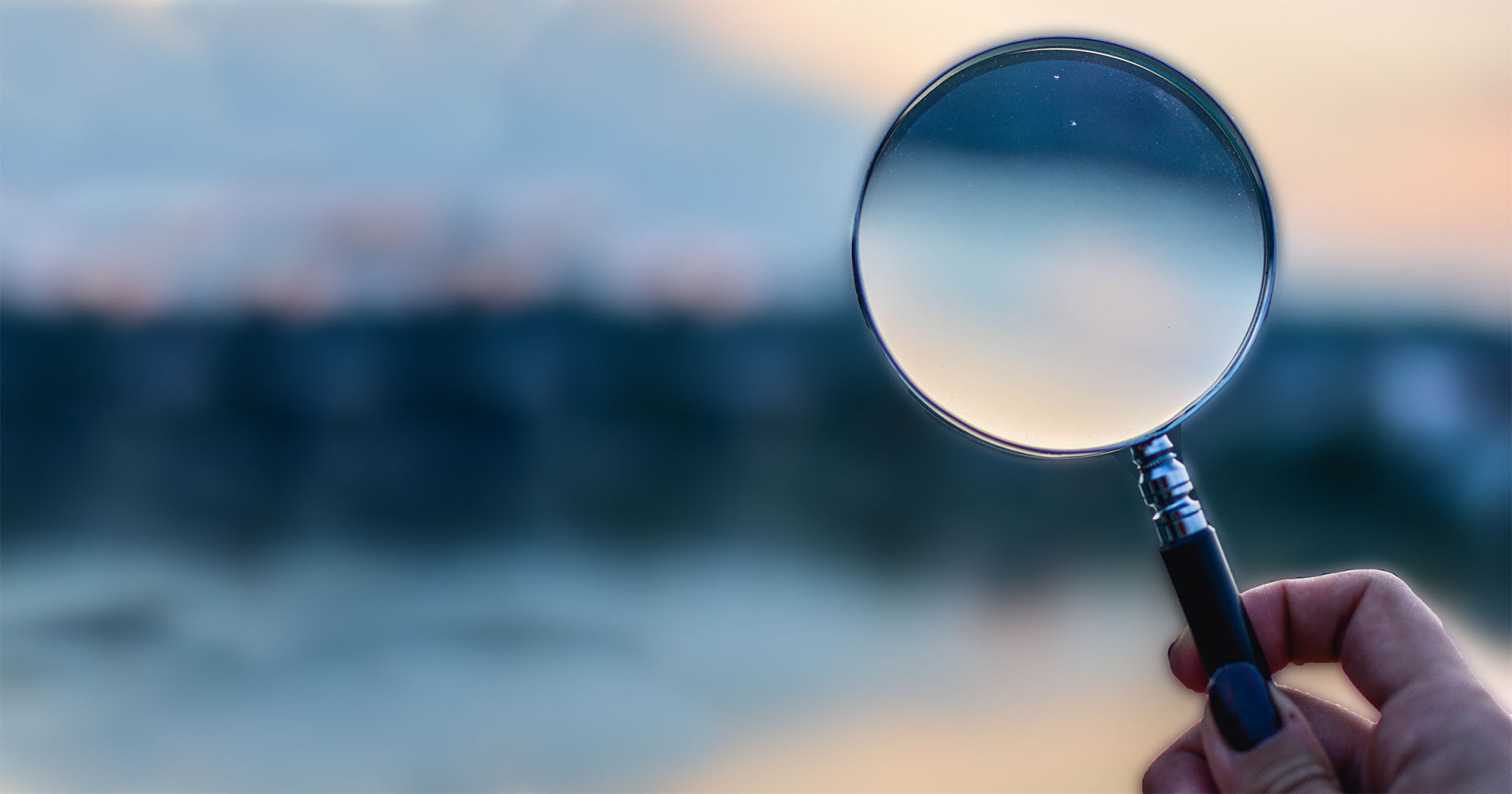 Picture of hand holding a magnifying glass in front of obscure environment